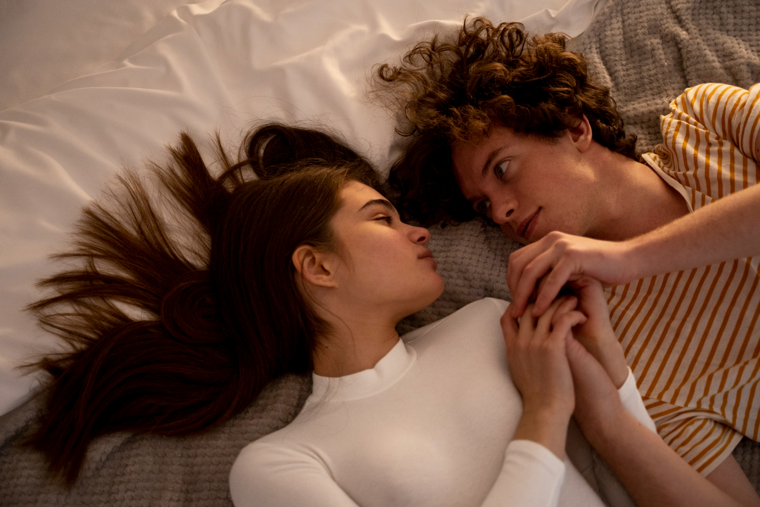 пара лежит на кровати и держится за руки